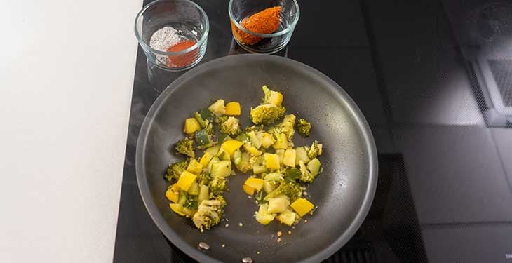 Garlic and vegetables being sauteed in a nonstick pan next to spices and soyrizo