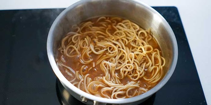 lomein noodles being sauced on a saute pan