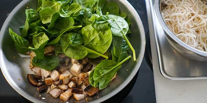 chicken mushrooms and spinach being cooked in a large stainless steel pan