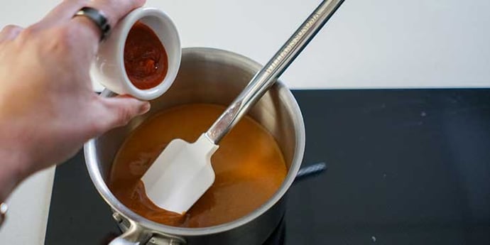 Thai-peanut sauce being made and reduced on a small sauce pan with a spatula inside the pot