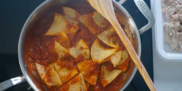 Tortilla chips added to the salsa in a stainless steel frypan