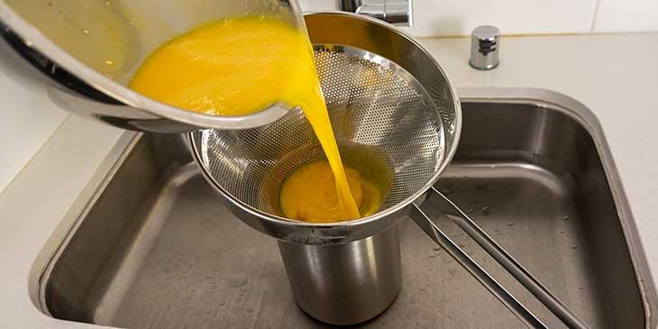 Straining blended eggs into a separate container in the kitchen sink
