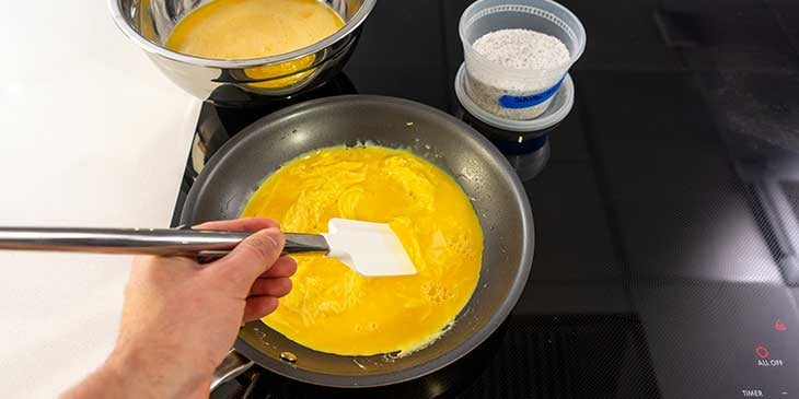 Scrambled eggs being cooked on an electric stove on a non-stick pan with a rubber spatula