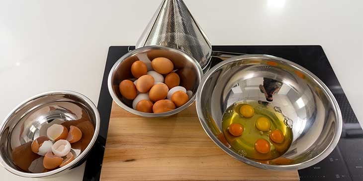 Cracking egg station set to crack eggs for meal prep with different bowls on top of a cutting board