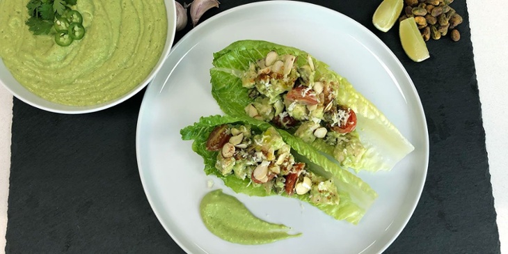 Keto guacatilllo chicken salad wrap plated on a white round plate placed on top of a black slab next to a green guacatillo sauce bowl