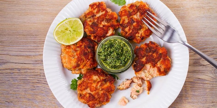 Keto Salmon Patties With Chimichurri Sauce plated on a white bowl with the chimichurri on the middle of the plate in a small glass bowl