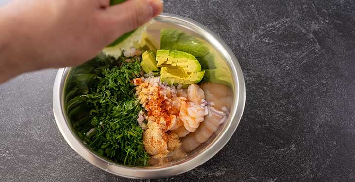 Mixed ingredients for keto shrimp avocado salad in a stainless steel bowl