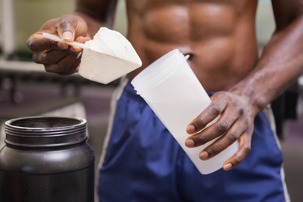 Mid section of a body builder holding a scoop of protein mix in gym