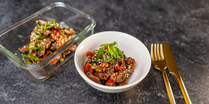 Paleo-Mongolian-Beef-Recipe plated on a white bowl and glass meal prep container next to golden silverware