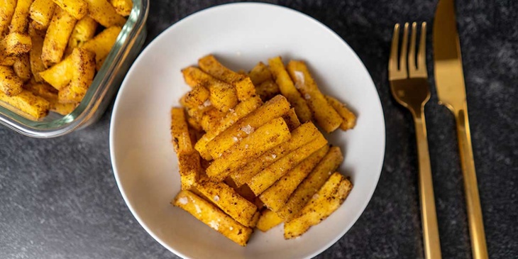 Paleo Spiced Roasted Butternut Squash Recipe plated on a white bowl and rectangle meal prep container served next to golden utensils on a black backdrop