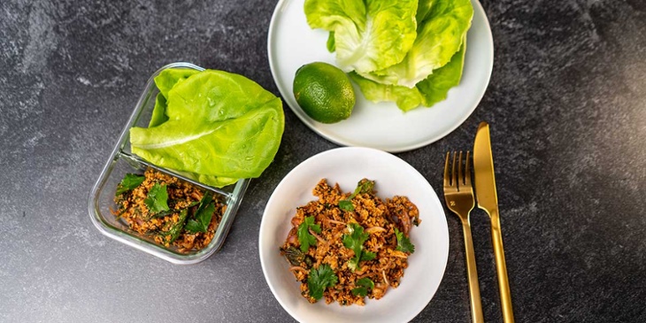 Paleo thai turkey larb recipe plated on a white bowl next to golden silverware and fresh lettuce on a round white plate