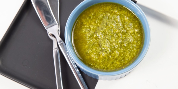 Pesto sauce on a ramekin bowl placed on top of a black and white platter next to butter knives