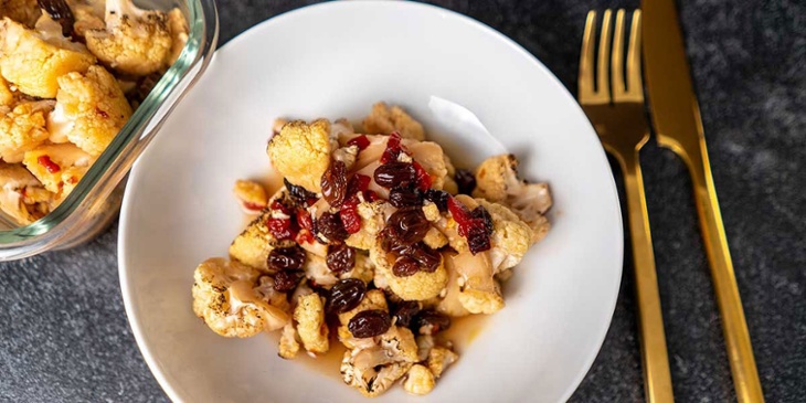 Roasted Paleo Cauliflower Agrodolce Sauce Recipe served on a white bowl next to gold utensils on a black backdrop