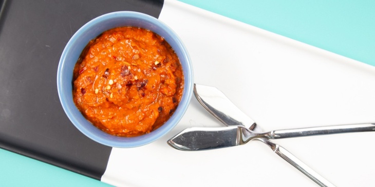 Romesco sauce on a blue ramekin container on top of a black and white platter next to butter knives