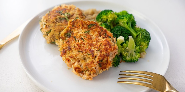 Best salmon cakes plated next to bright green broccoli on a white plate with golden silverware