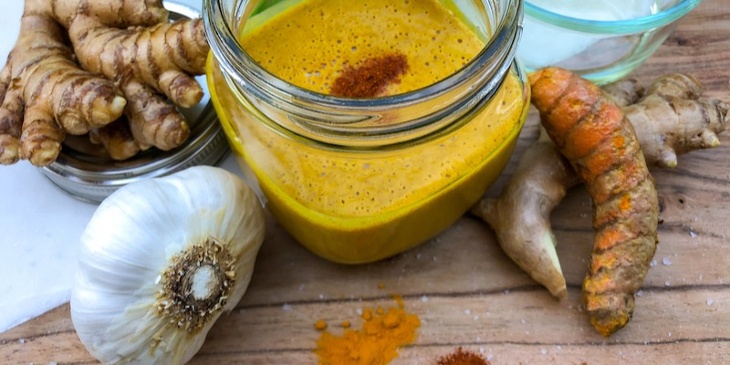 Trifecta Keto Almond-Turmeric Dressing on a mason jar surrounded by fresh ginger garlic and turmeric root