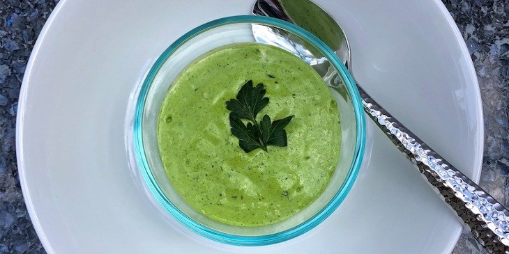 Keto herb crema plated on a round ramekin placed on top of a white bowl next to a silver spoon