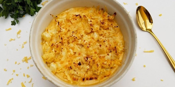 keto cauliflower mac and cheese plated on a white bowl next to a golden spoon