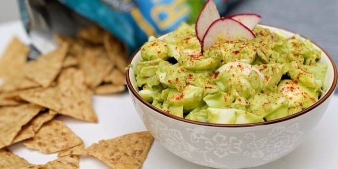 Healthy avocado egg salad plated on a white bowl with chips coming out of a bag on the side