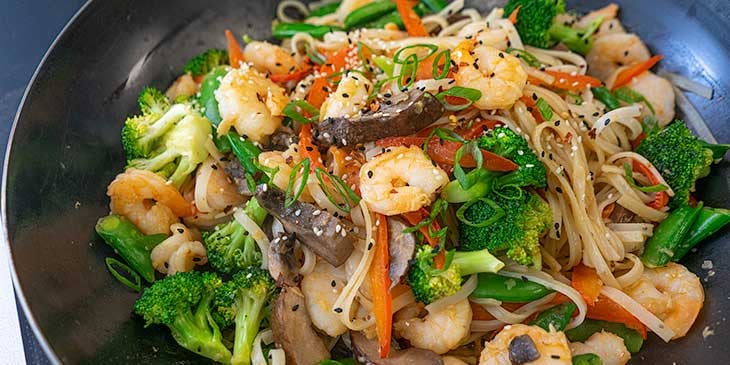 cooking shrimp noodle stir fry in wok for meal prep 