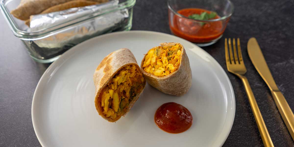 breakfast burrito recipe plated with red salsa next to golden silverware and on a rectangular glass meal prep container
