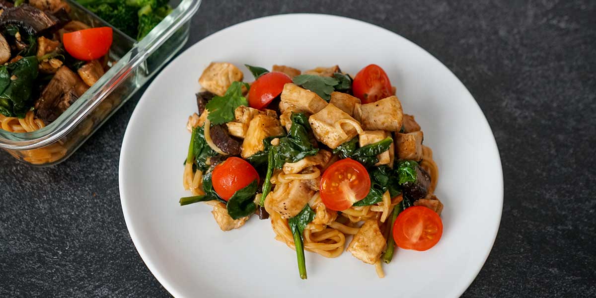 Chilaquiles Chicken Recipe plated on a white porcelain plate next to a glass meal prep containers on top of a black mate background