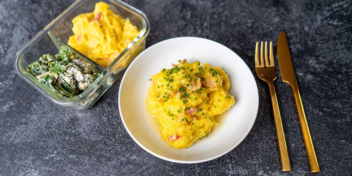 Paleo Creamy Bacon & Spaghetti Squash Recipe served on a white round plate and a rectangular meal prep container with golden silverware on top of a black background