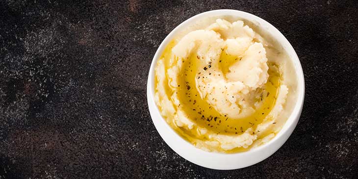 Mashed 50/50 potato plated on a small white bowl on a black background
