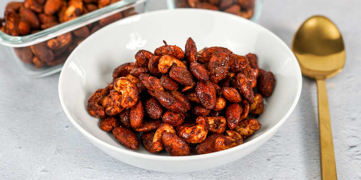Paleo Roasted Spiced Nuts Recipe plated on a white bowl and also on meal prep containers in the background