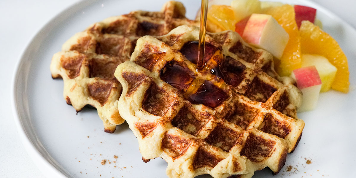 Maple Cinnamon Sweet Potato Waffle Recipe served with fruit on the side and syrup being poured on top